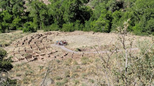Aerial view of a circular stone structure surrounded by greenery, with a small group of people in the center.