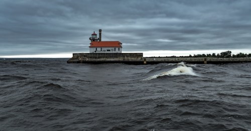 A lighthouse on a pier stands against a dark, cloudy sky with choppy waves in the foreground.