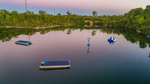 A serene lake at sunset, featuring floating docks and buoys surrounded by lush greenery.