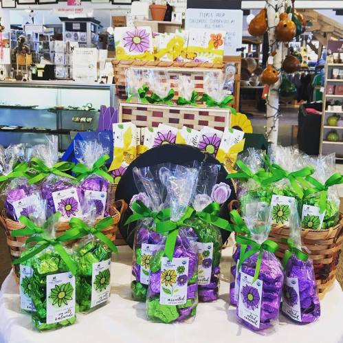 Colorful gift baskets filled with treats, wrapped in cellophane and tied with green ribbons, displayed in a shop.