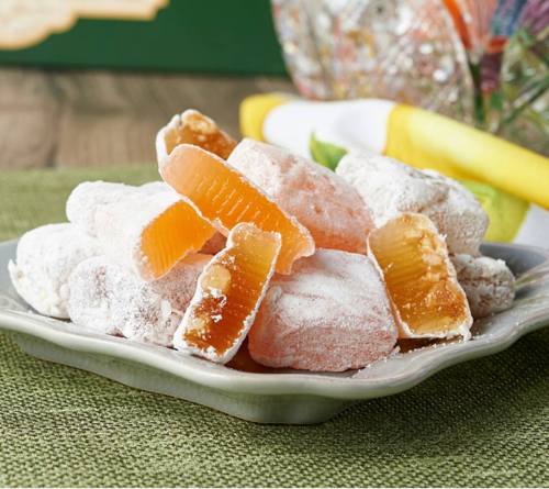 A plate of colorful, powdered fruit jellies in various shapes, including orange and pink, on a textured green surface.