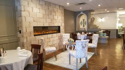 Cozy restaurant interior featuring a stone wall, modern fireplace, and elegantly set tables with floral chairs.