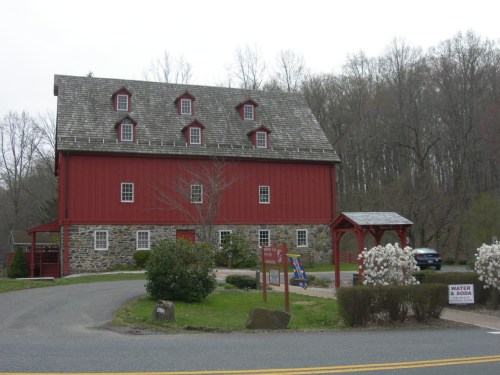 A red barn-style building with a stone foundation, surrounded by greenery and a gravel path.
