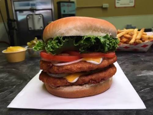 A towering chicken sandwich with lettuce, tomato, and cheese, served with a side of fries.