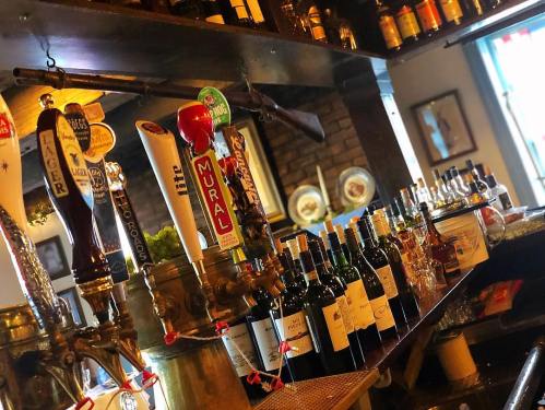 A bar shelf displaying various beer taps and bottles of wine, with a rustic wooden backdrop and decorative items.