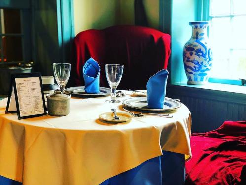 A beautifully set dining table with blue napkins, glassware, and a menu, beside a decorative vase and cozy seating.