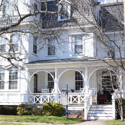 A charming white house with a porch featuring arched supports, surrounded by trees and greenery.
