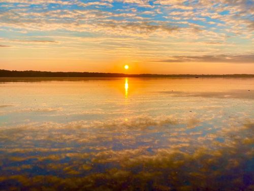 A serene sunset over a calm lake, with vibrant colors reflecting on the water's surface and soft clouds in the sky.