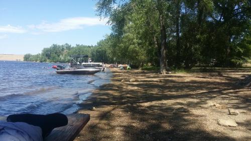 A serene lakeside scene with a boat docked near a sandy shore, surrounded by trees and people enjoying the outdoors.