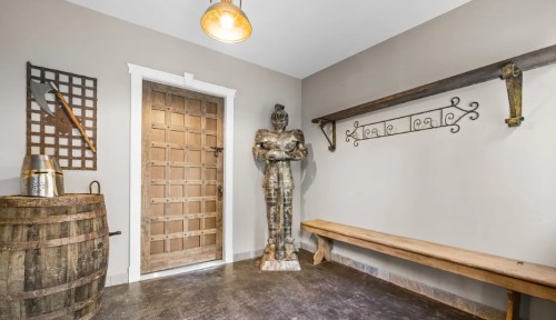 A hallway featuring a wooden door, a knight statue, a barrel, and a bench against a neutral wall.