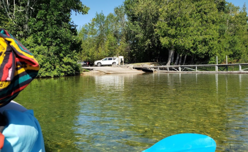 A serene lake view with a dock, surrounded by trees, and a vehicle parked nearby on a sunny day.