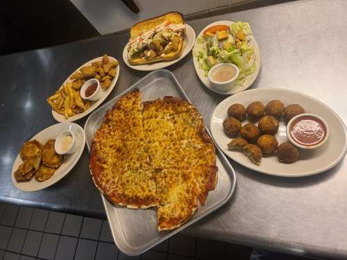 A spread of food including pizza, salad, fried chicken, fries, and appetizers on a metal table.