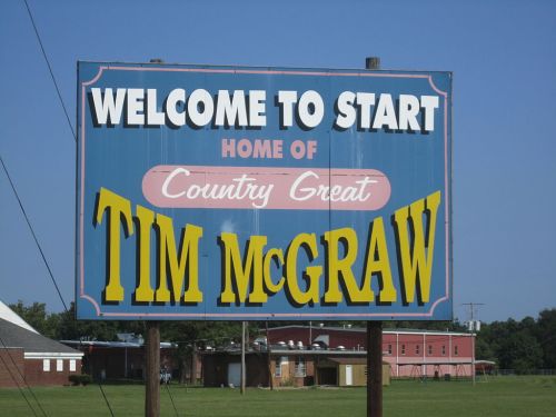 Sign welcoming visitors, stating "Welcome to Start, Home of Country Great Tim McGraw." Bright blue background with bold text.