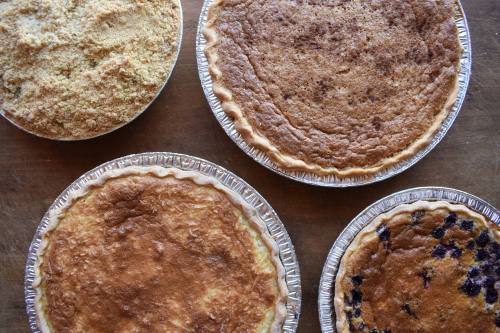 Four different pies on a wooden surface, including a crumb-topped pie and a blueberry pie.