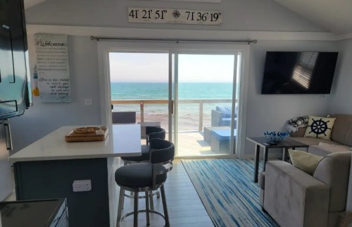 Cozy beach house interior with ocean view, featuring a living area, kitchen, and sliding glass doors to a deck.