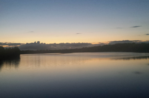A serene lake at dusk, reflecting a colorful sky with clouds and a calm water surface.