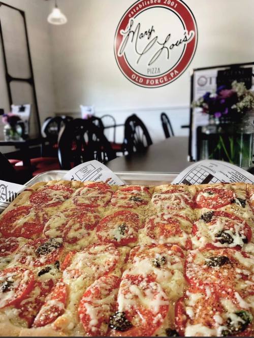 A tray of pizza topped with cheese and tomatoes, with a restaurant logo in the background.