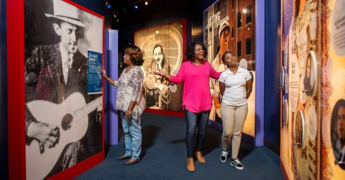 Three women explore an exhibit, engaging with displays featuring historical figures and information on the walls.