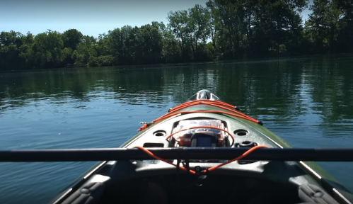 View from a kayak on calm water, surrounded by lush green trees and a clear blue sky.