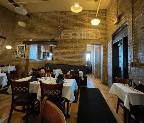 Interior of a cozy restaurant with brick walls, white tablecloths, and a doorway leading to another area.