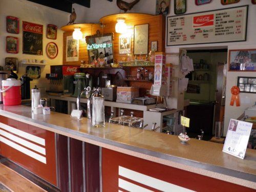 A vintage diner counter with a soda fountain, menu board, and nostalgic decor, creating a cozy atmosphere.