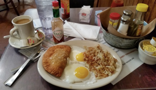A breakfast plate with two eggs, hash browns, and a pastry, alongside coffee and various condiments on a table.