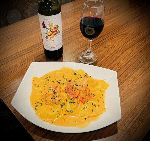A plate of creamy pasta with shrimp, garnished with herbs, alongside a glass of red wine and a wine bottle.