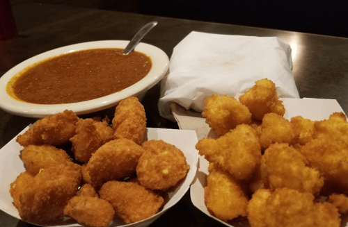 A bowl of brown chili next to two servings of golden fried snacks on a table.