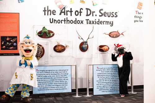 Two costumed characters stand beside displays of whimsical taxidermy art inspired by Dr. Seuss.