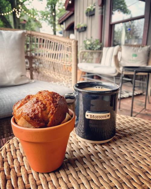 A cozy café scene featuring a muffin in a flower pot and a cup of coffee on a woven table.
