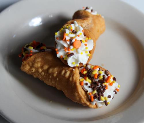 Two cannoli filled with cream and topped with colorful sprinkles, resting on a white plate.