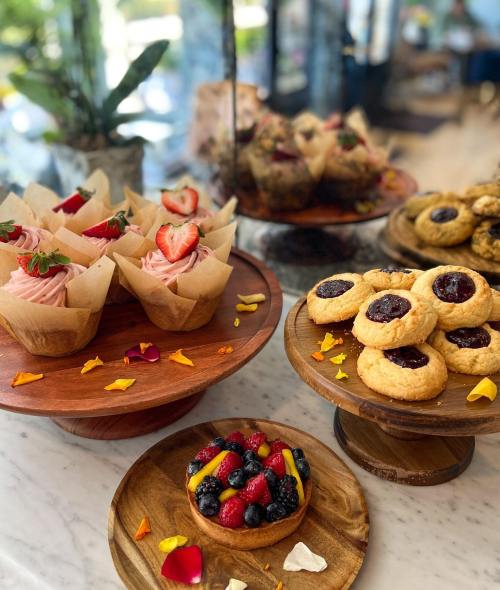 A display of desserts featuring cupcakes with strawberries, cookies with jam, and a bowl of mixed berries.