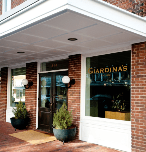 Exterior of Giardina's restaurant, featuring a brick facade, large windows, and decorative planters at the entrance.