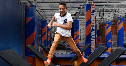 A young boy jumps joyfully on trampolines in a vibrant indoor trampoline park.