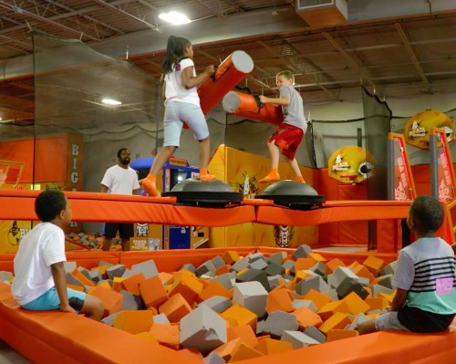 Children play on a foam pit obstacle course, while others watch from the edge, in a vibrant indoor activity center.