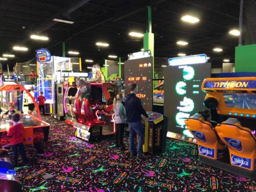 A colorful arcade filled with various games and children playing, featuring bright lights and a vibrant floor design.
