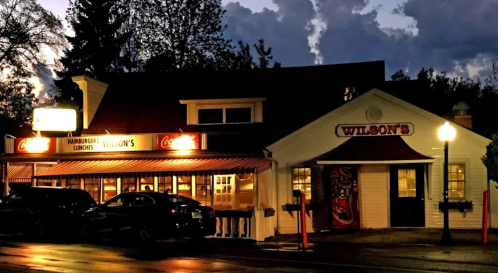 A cozy restaurant named Wilson's, illuminated at night, with a sign for hamburgers and lunch.
