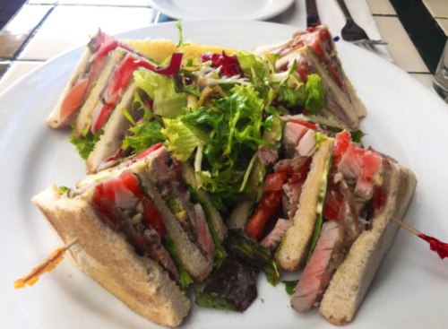 A plate with a club sandwich cut into triangles, surrounded by a fresh green salad.