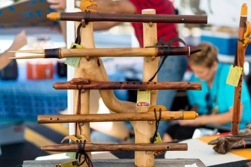 A display of wooden flutes arranged on a stand, with a blurred background of people at a market.