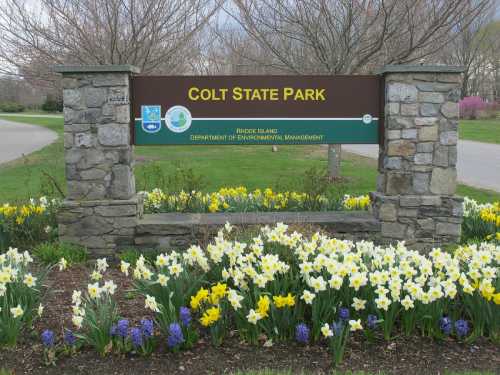 Sign for Colt State Park in Rhode Island, surrounded by colorful flowers and greenery.