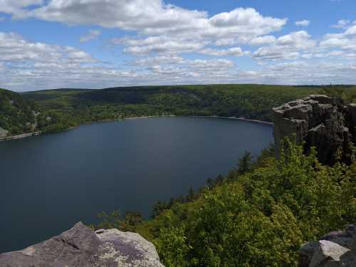 A serene lake surrounded by lush greenery and rocky cliffs under a partly cloudy sky.