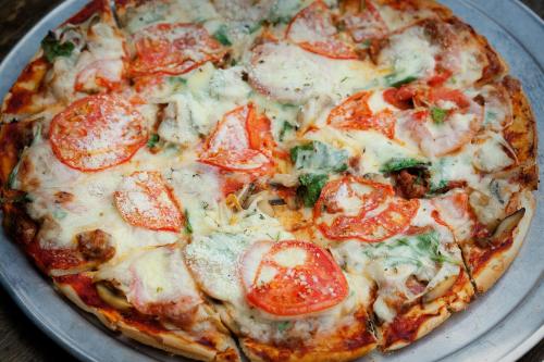 A freshly baked pizza topped with cheese, tomatoes, mushrooms, and greens on a metal tray.
