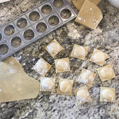 Homemade ravioli on a granite countertop, with pasta dough and a ravioli cutter nearby.