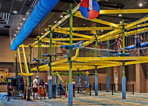 Indoor adventure park featuring a colorful ropes course with various obstacles and children playing below.