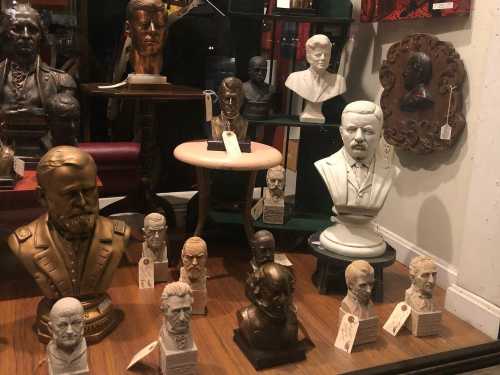 A display of various busts and sculptures, featuring historical figures, arranged on a wooden surface.