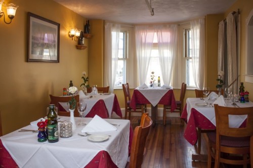 Cozy restaurant interior with tables set for dining, featuring white tablecloths and warm yellow walls.