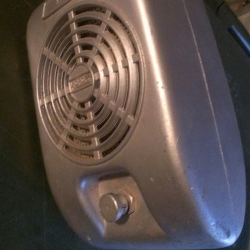 A vintage metal fan with a circular grille and a control knob, resting on a dark surface.