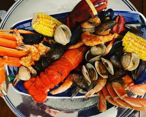 A colorful seafood platter featuring lobster, crab, shrimp, mussels, clams, and corn on a decorative blue dish.