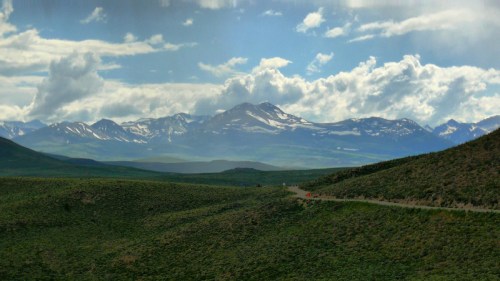 A scenic view of mountains under a cloudy sky, with green hills in the foreground and snow-capped peaks in the distance.