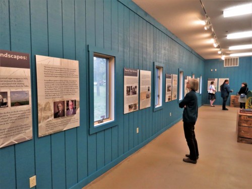 A person examines informational displays on blue walls in a museum, with others visible in the background.